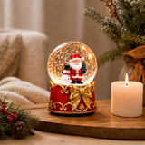 Glob de Zăpadă Premium de Crăciun cu Moș Crăciun, Bază tip Cutie Cadou cu Fundă Aurie, Muzică, Lumină LED și Efect de Ninsoare – 15 × 10 cm - in context de utilizare